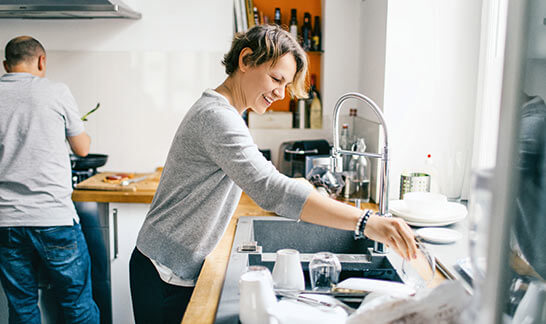 Une femme se tient debout dans sa cuisine et fait la vaisselle