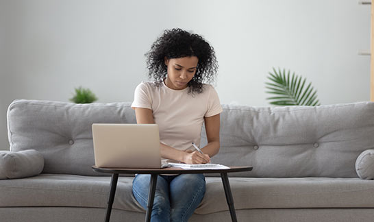 Bonität  - Junge Frau sitzt auf dem Sofa mit dem Laptop und Dokumente